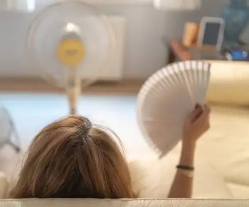 Mulher se abanando no sofá contra o calor da menopausa no verão